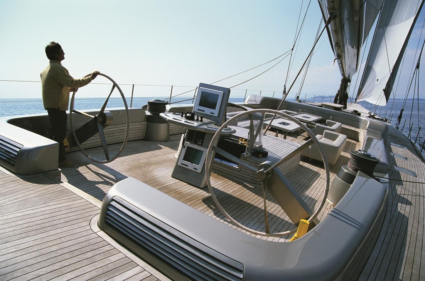 a person standing on a deck with a laptop and a large sailboat aboard SYL Yacht for Sale