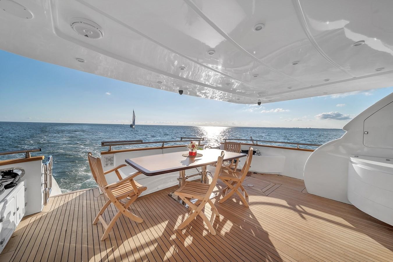 a deck with a table and chairs on it by the ocean aboard DOMINIC Yacht for Sale