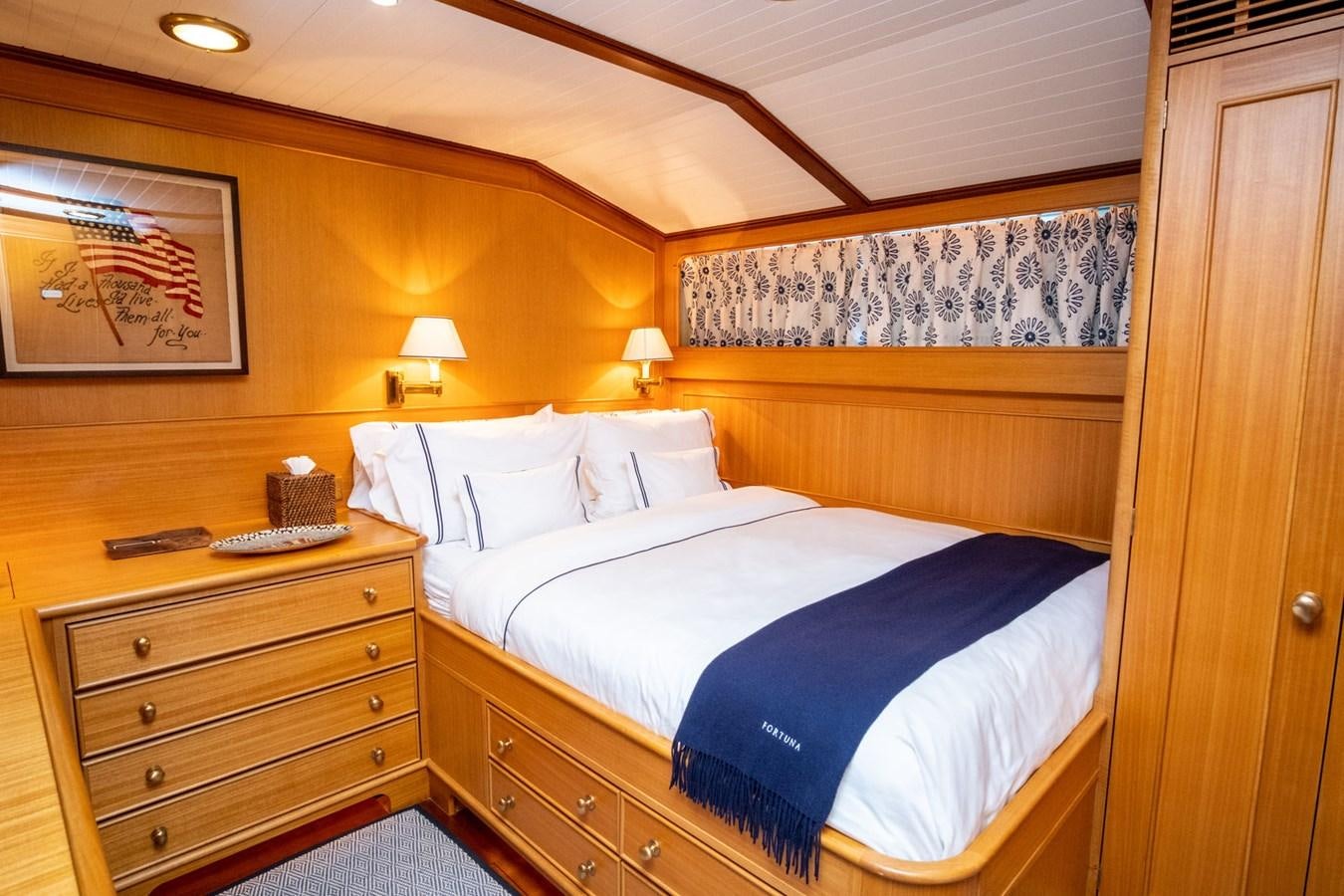 a bed with a blue bedspread and a wooden headboard aboard FORTUNA Yacht for Sale
