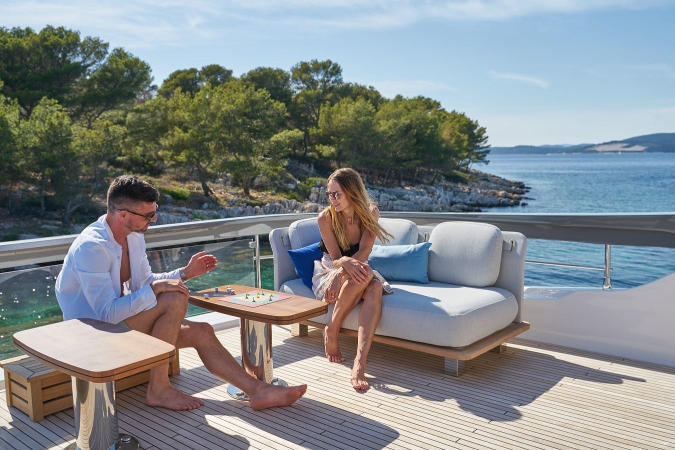 a man and woman sitting on a couch on a deck by the water aboard VIVA Yacht for Sale