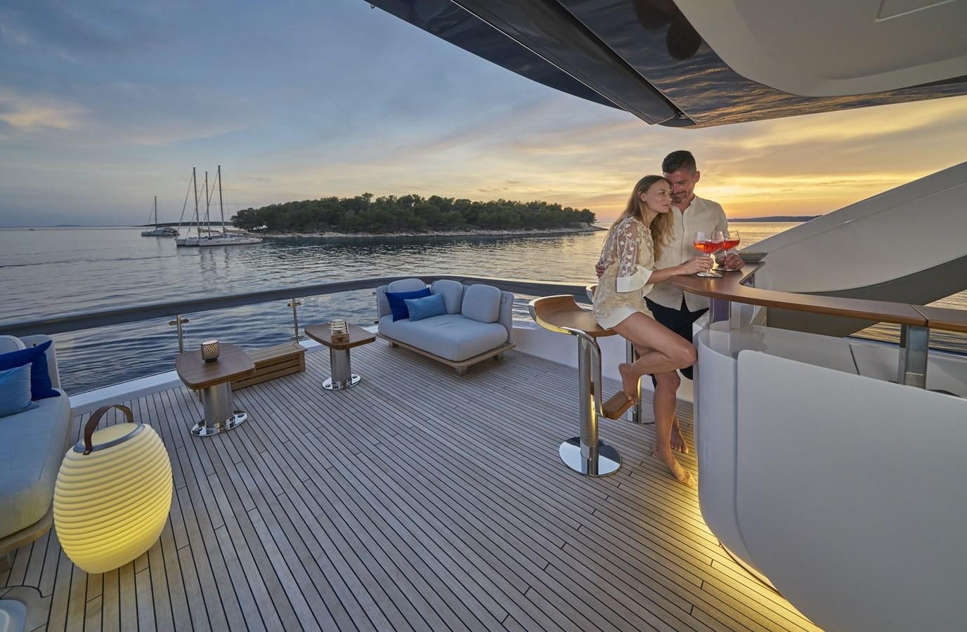 a man and woman sitting on a deck with a drink and a boat in the background aboard VIVA Yacht for Sale