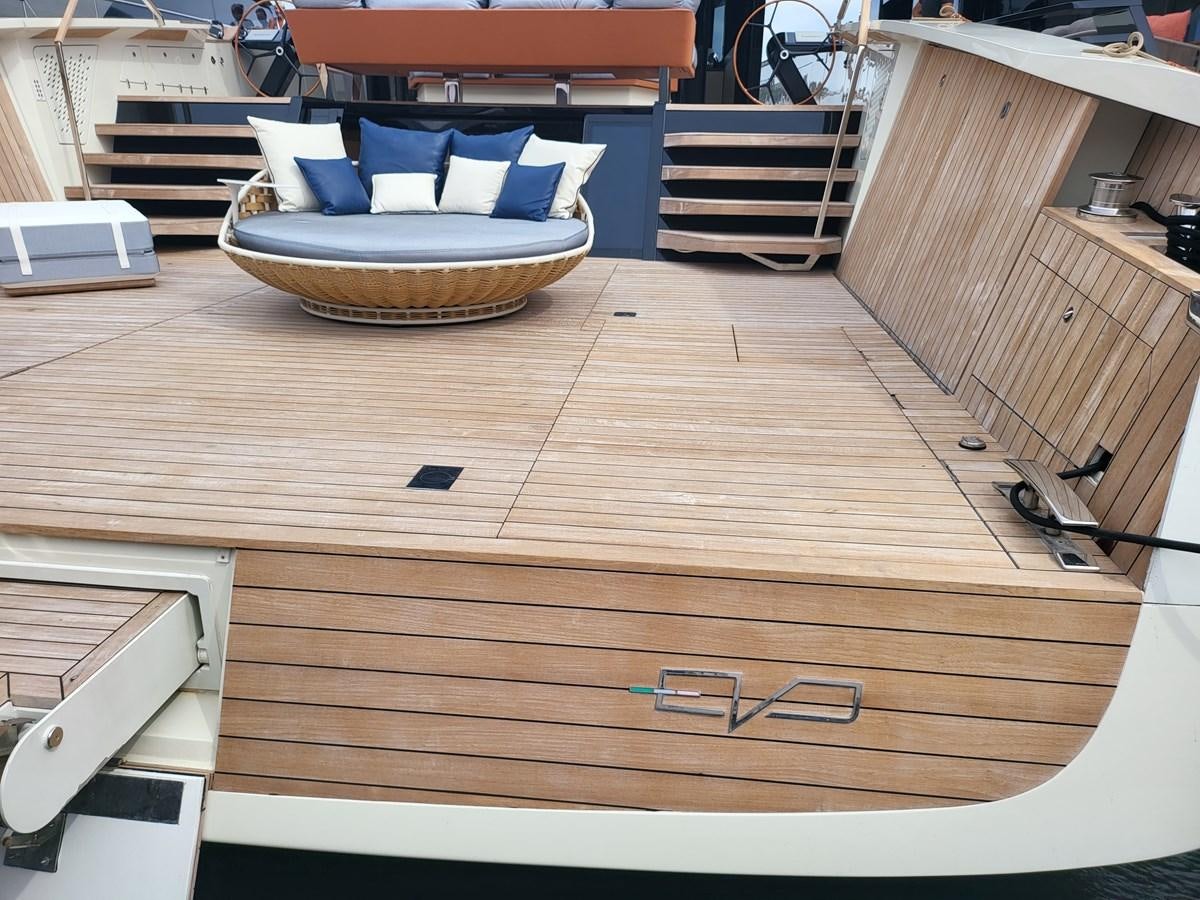 a wooden deck with a round table and a blue pillow on it aboard EVO V8  Yacht for Sale