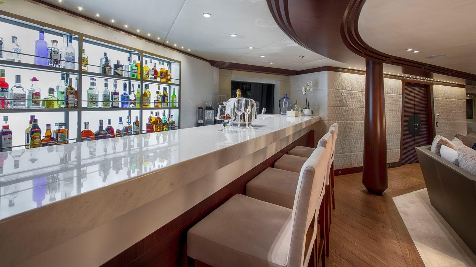 a room with a bar and a table with chairs and bottles aboard KATINA Yacht for Charter