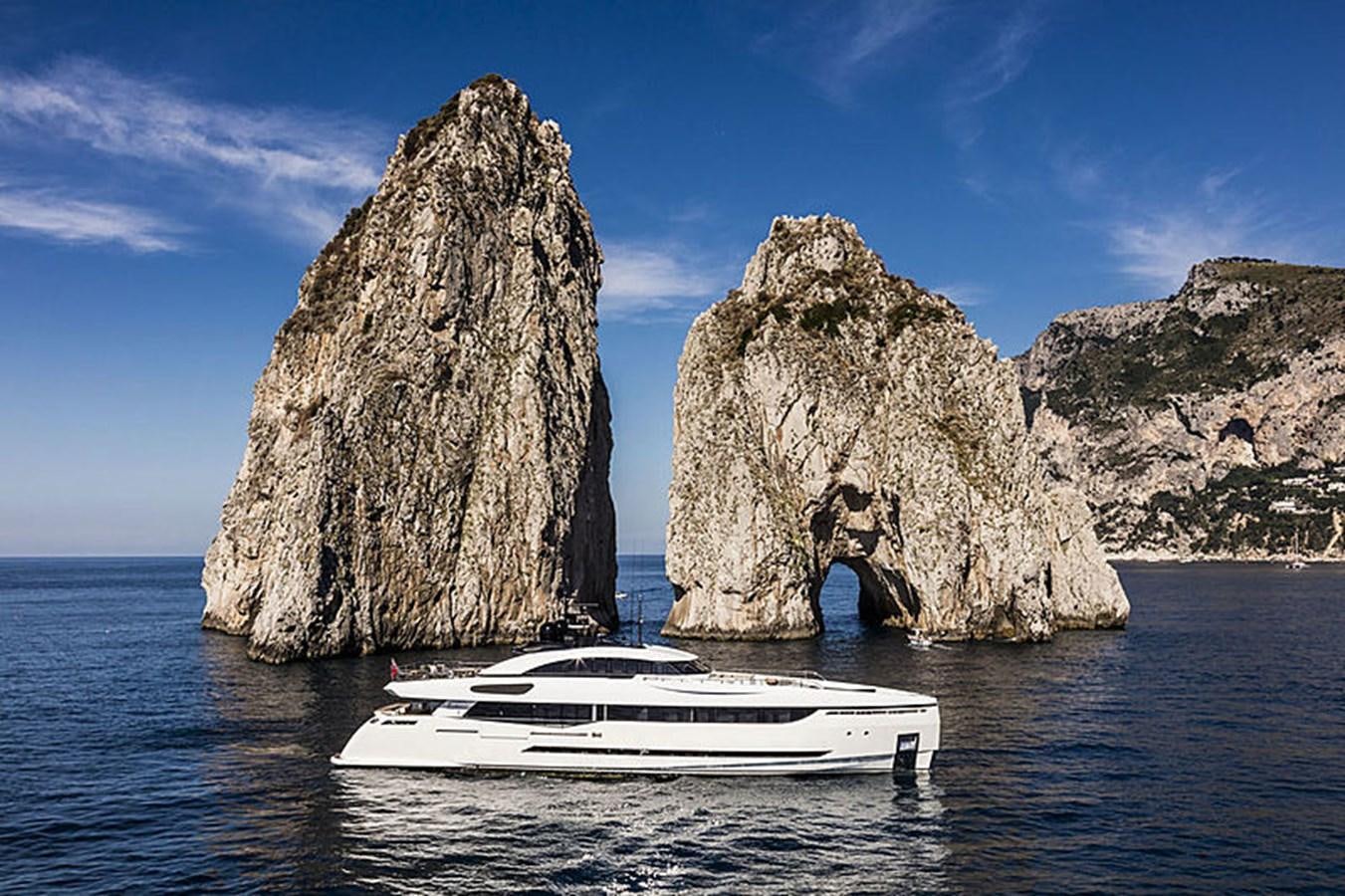a boat in the water by large rocks with Faraglioni in the background aboard NEXT Yacht for Sale