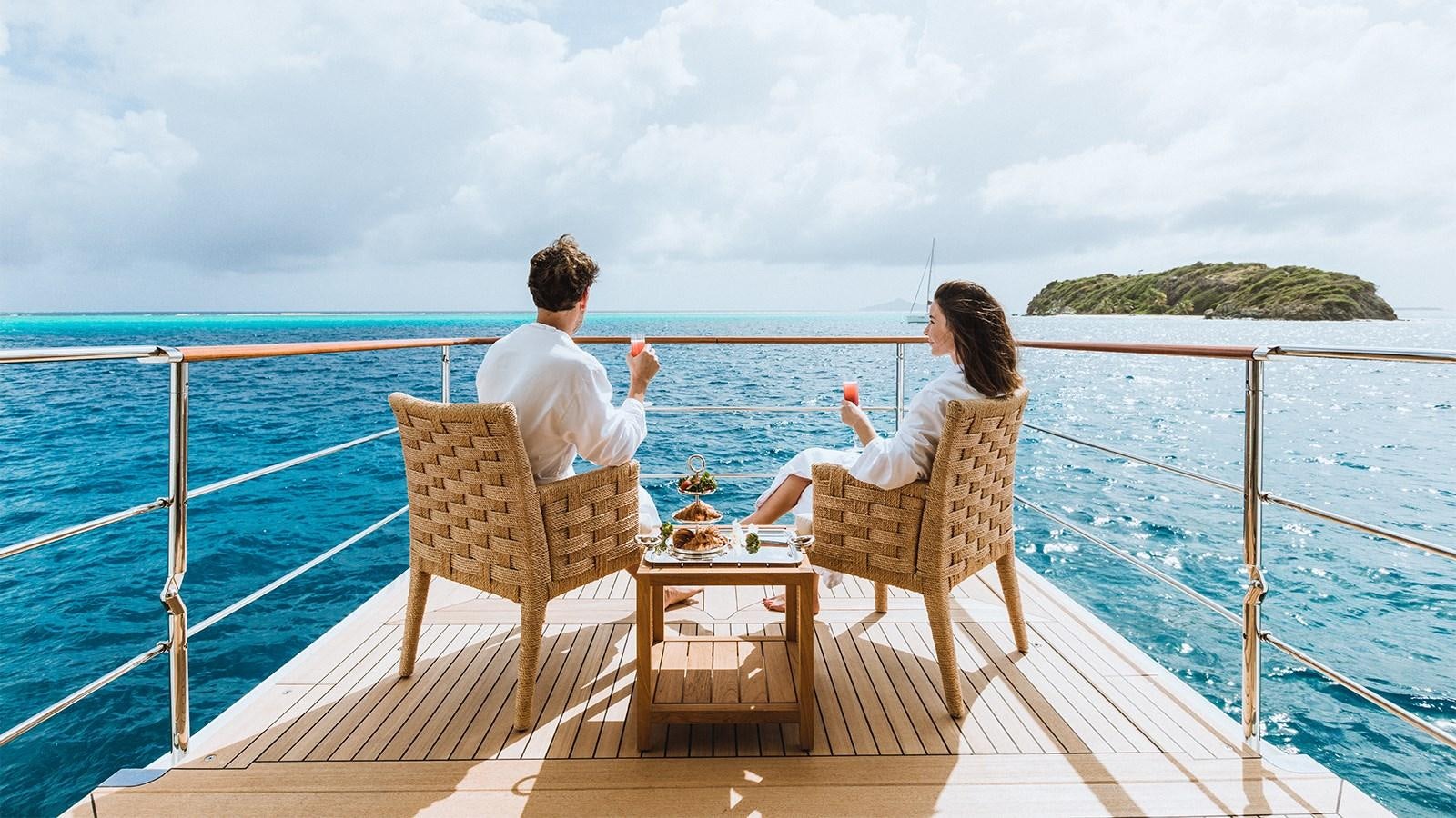 a man and woman sitting on a bench on a dock over the ocean aboard CLELIA III Yacht for Charter