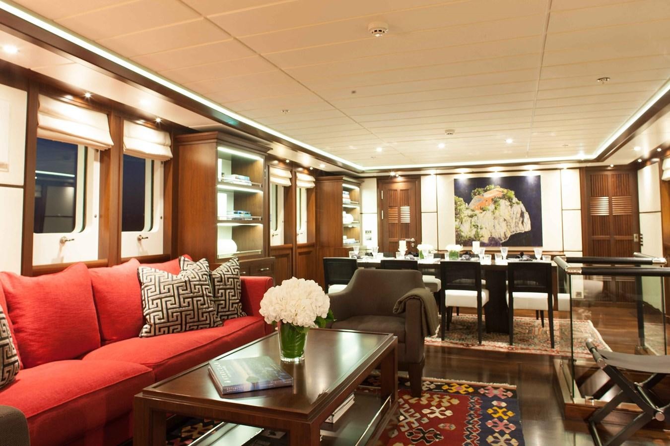 a living room with a red couch and a table with white flowers aboard ICE LADY Yacht for Sale