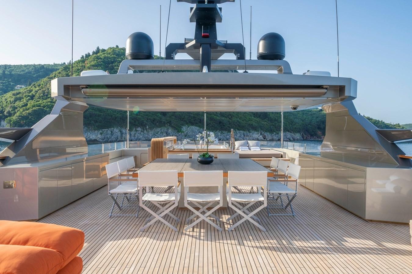 a large white and black deck with a round table and chairs and a large white building with a aboard MAVERICK Yacht for Sale