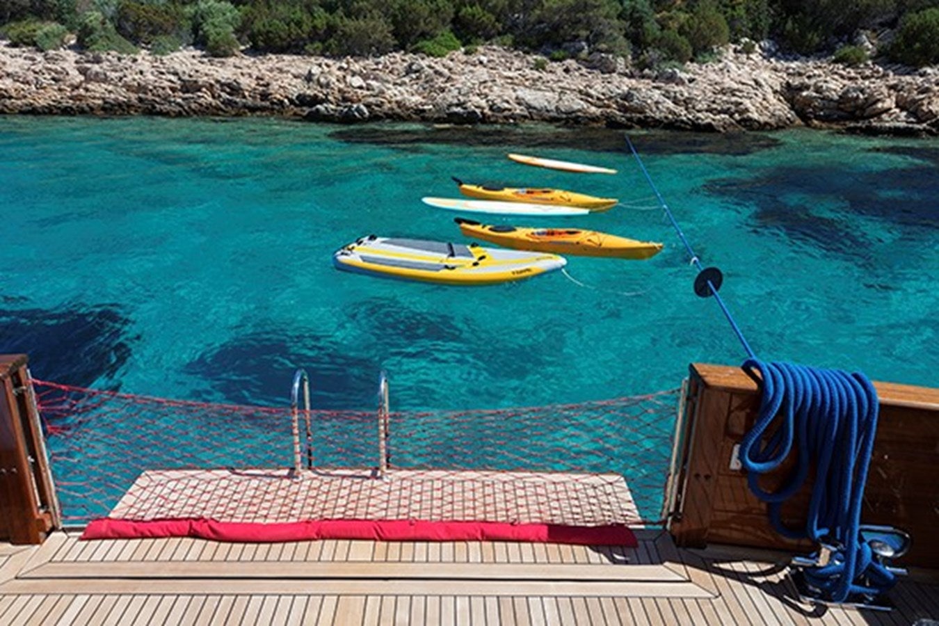 a chair and a table on a beach with boats in the water aboard DARWIN Yacht for Sale