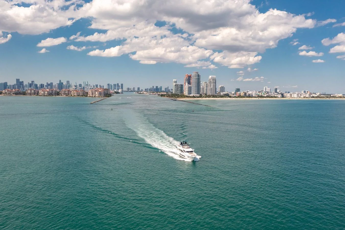 A yacht cruises through clear blue waters with a cityscape in the background. aboard SUNSEEKER Yacht for Sale