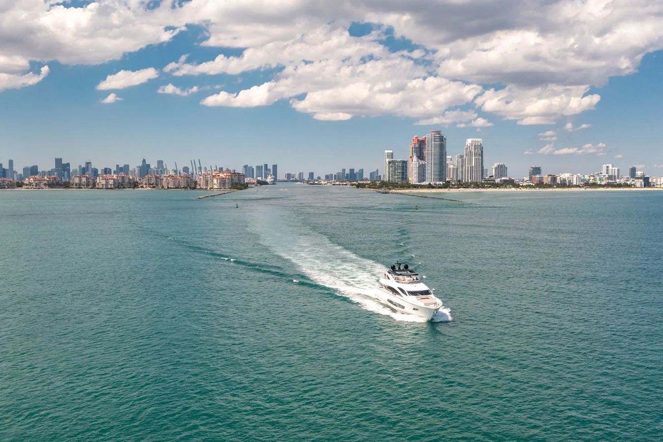 A sleek yacht cruises through turquoise waters with a city skyline in the background. aboard SUNSEEKER Yacht for Sale