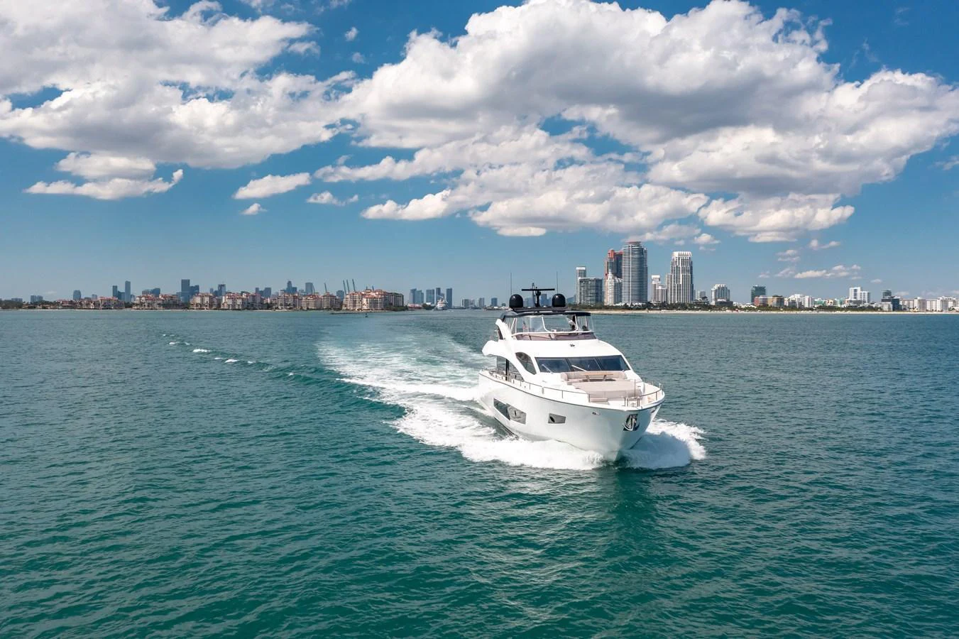 A sleek yacht cruises through calm waters with a cityscape in the background. aboard SUNSEEKER Yacht for Sale