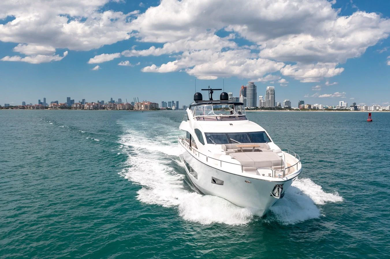 A sleek yacht cruises through clear blue waters with a city skyline in the background. aboard SUNSEEKER Yacht for Sale