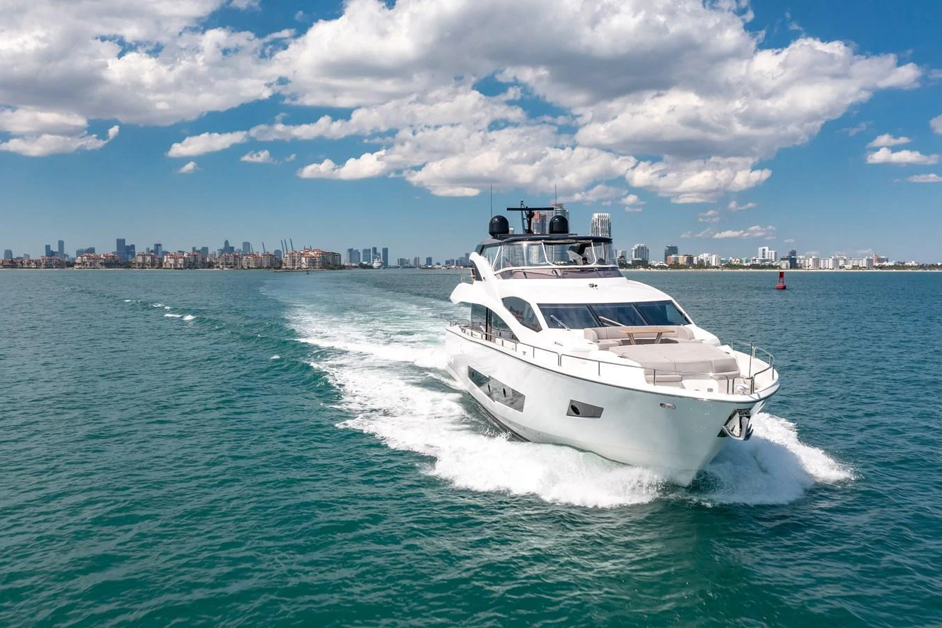 A sleek yacht cruises through clear blue waters with a cityscape in the background. aboard SUNSEEKER Yacht for Sale