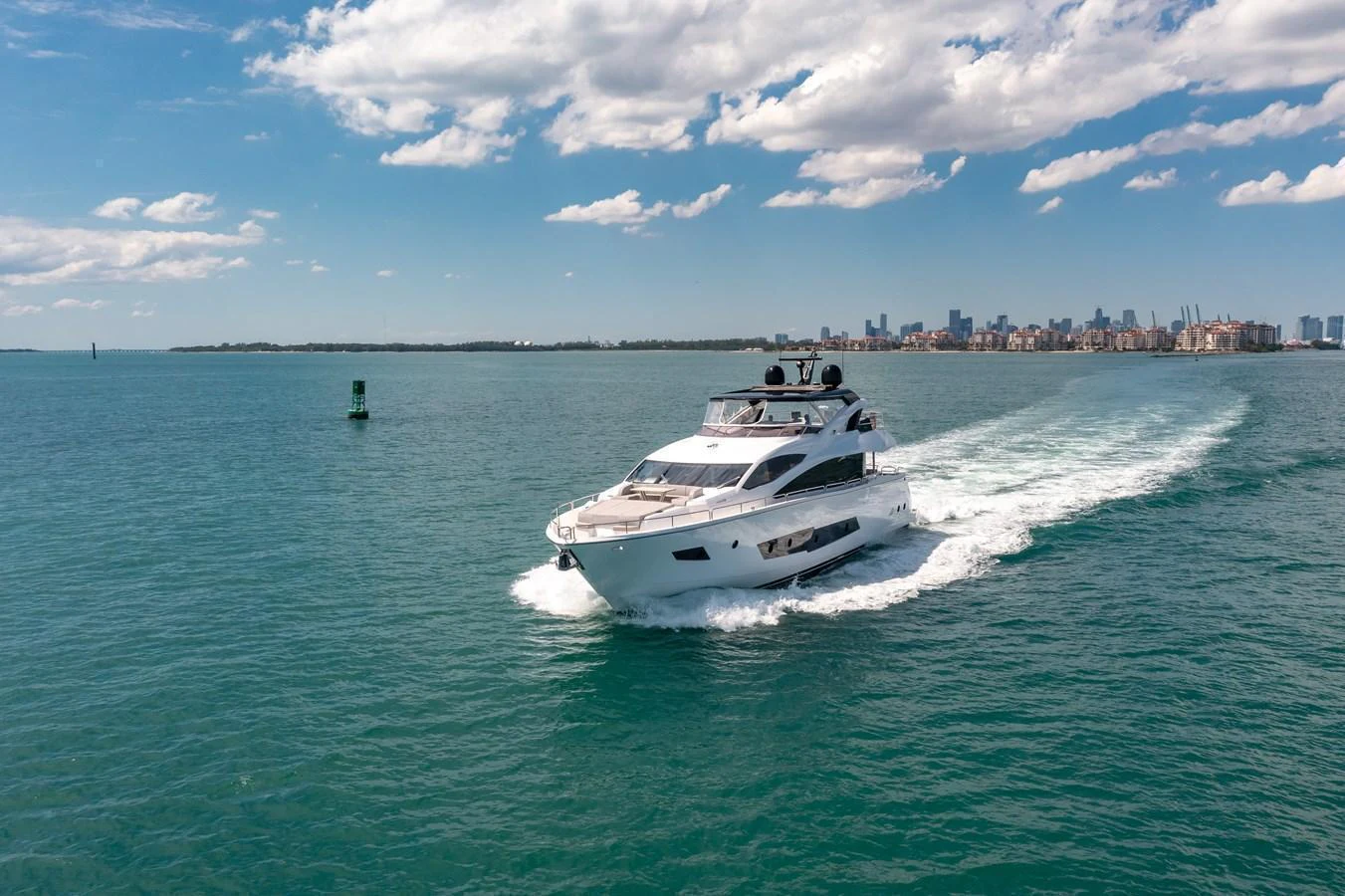 A sleek yacht cruises through calm waters with a cityscape in the background. aboard SUNSEEKER Yacht for Sale