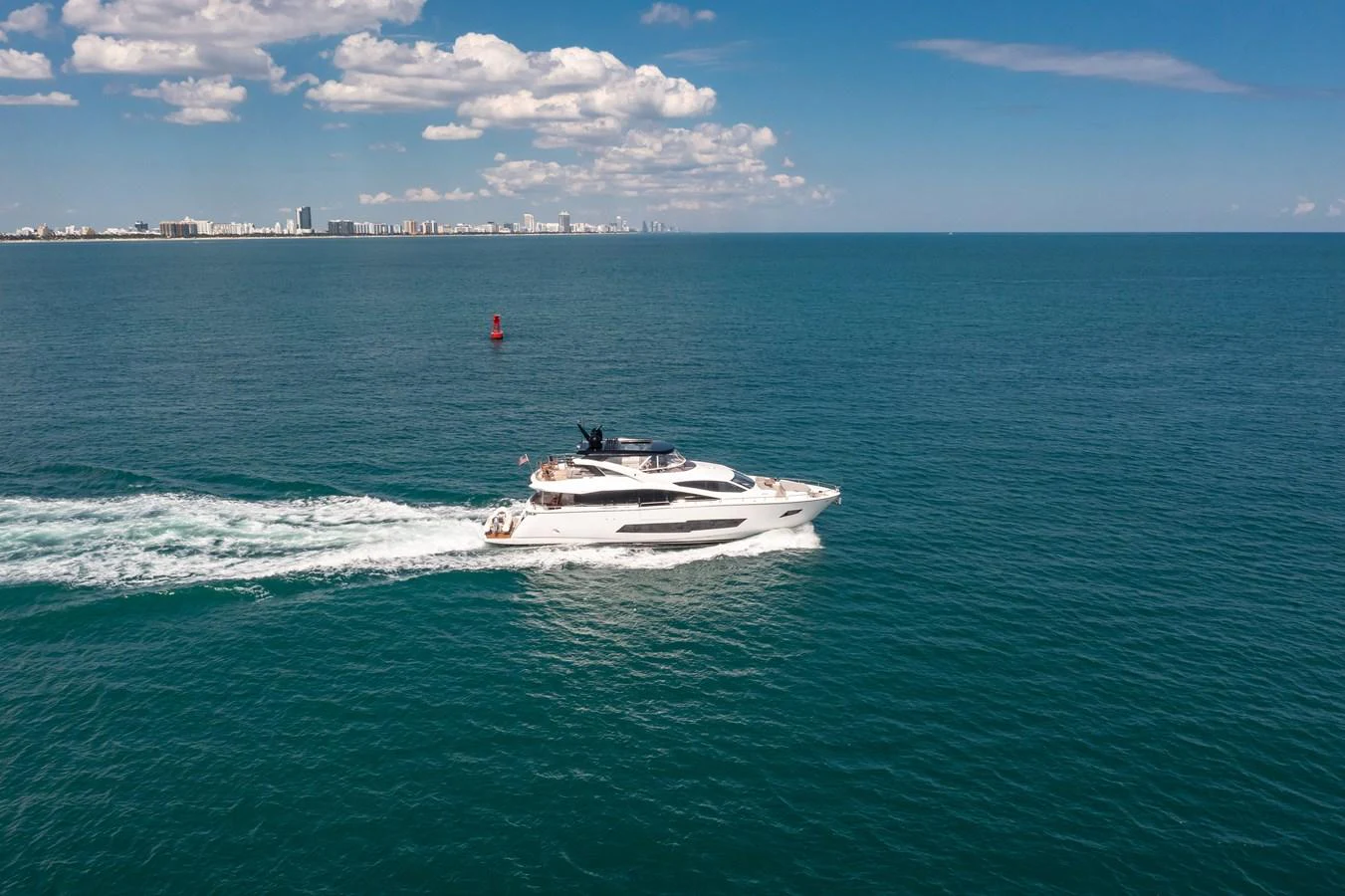 A sleek yacht cruises through calm, blue waters with a cityscape in the background. aboard SUNSEEKER Yacht for Sale