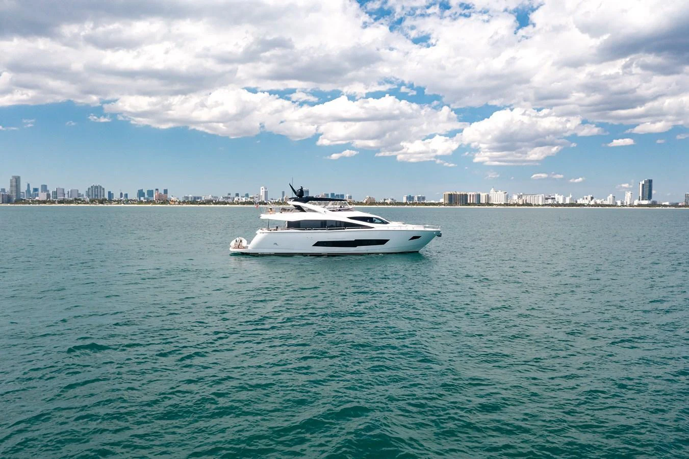 A sleek and modern yacht cruises gracefully on calm waters with a cityscape in the background. aboard SUNSEEKER Yacht for Sale