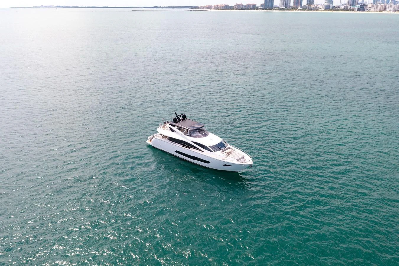 A sleek yacht cruises through calm waters with a cityscape in the background. aboard SUNSEEKER Yacht for Sale