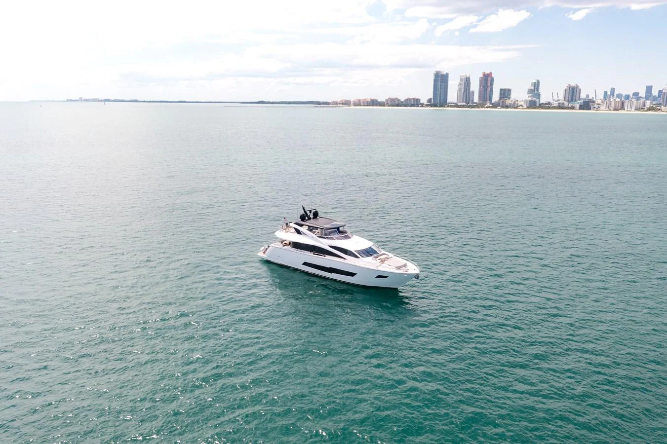 A sleek yacht cruises on calm waters with a city skyline in the background. aboard SUNSEEKER Yacht for Sale