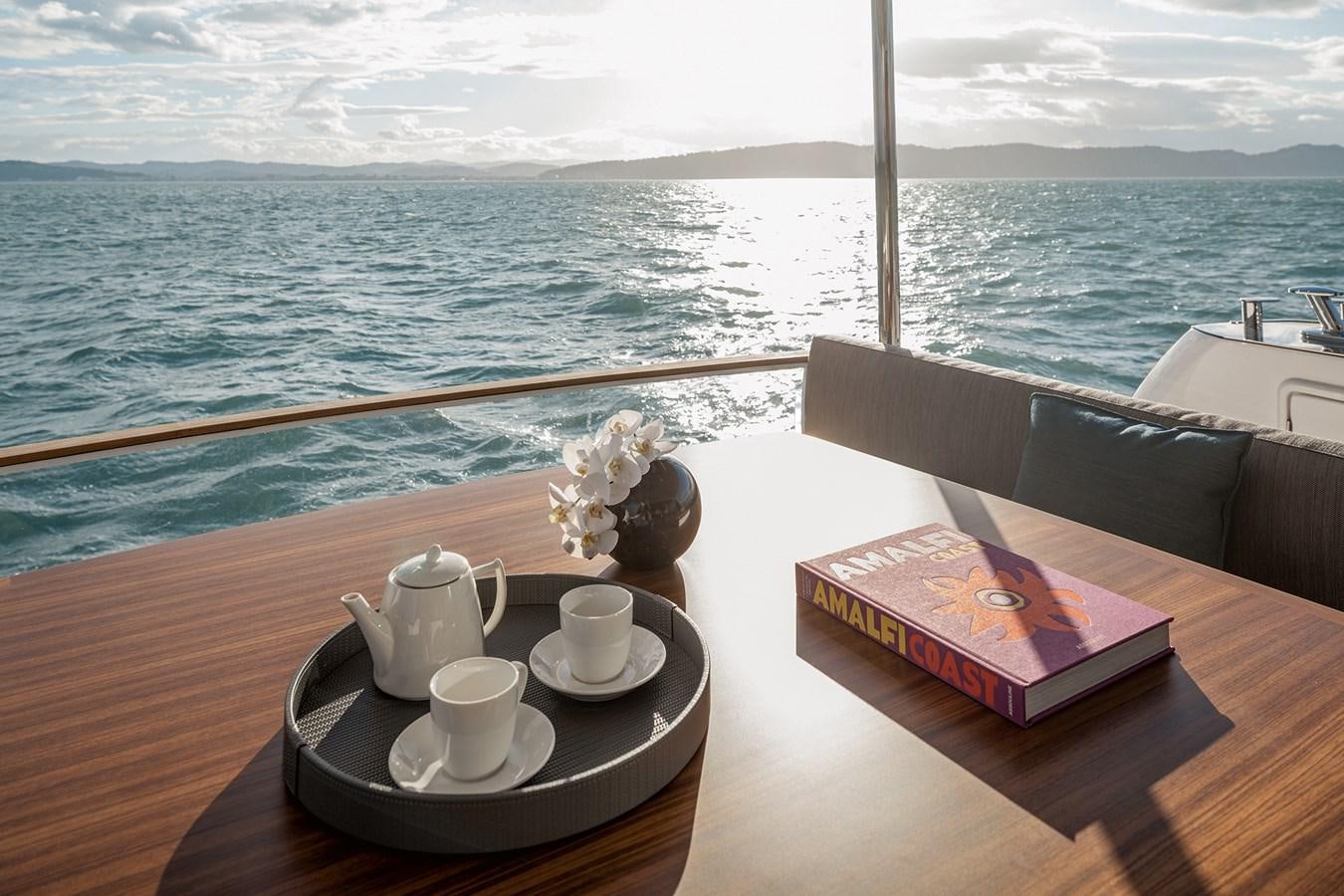 a table with cups and a book on it by a window with a view of the ocean and aboard 66 MAGELLANO Yacht for Sale