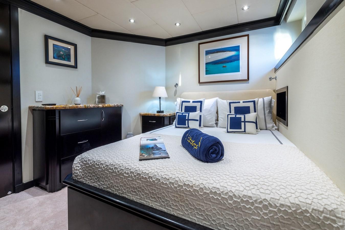 a bed with a white comforter and pillows in a room with a desk and a television aboard L'ALBATROS Yacht for Sale