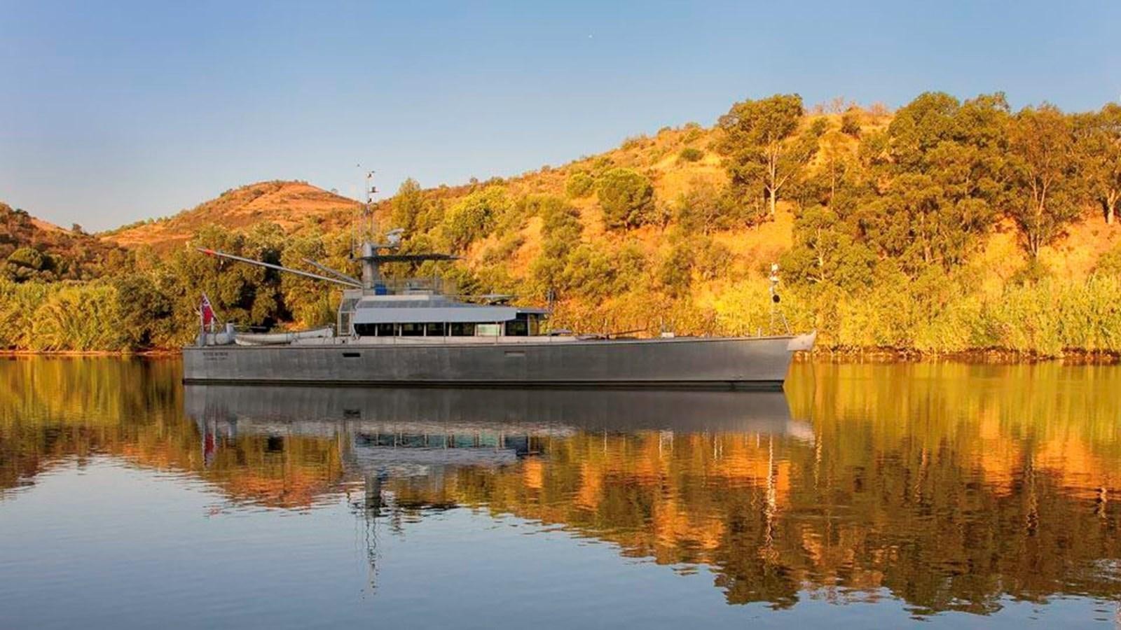 a building on a dock in a lake with trees and mountains in the background aboard WIND HORSE Yacht for Sale
