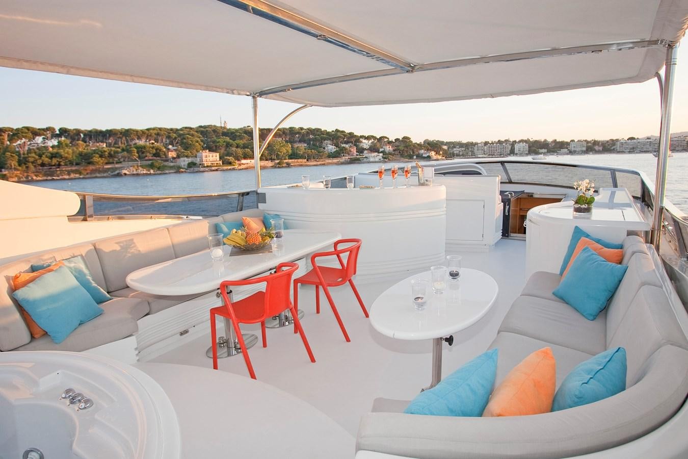 a large white lounge chair next to a table with a white table and red chairs on it aboard COCA VI Yacht for Sale