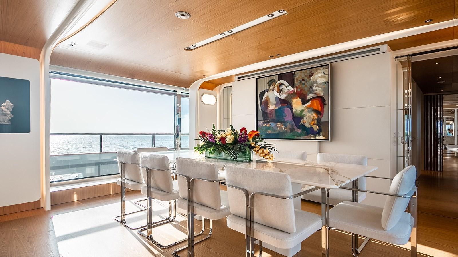 a room with white chairs and a table with white chairs and a large window with a view of aboard KOJU Yacht for Sale