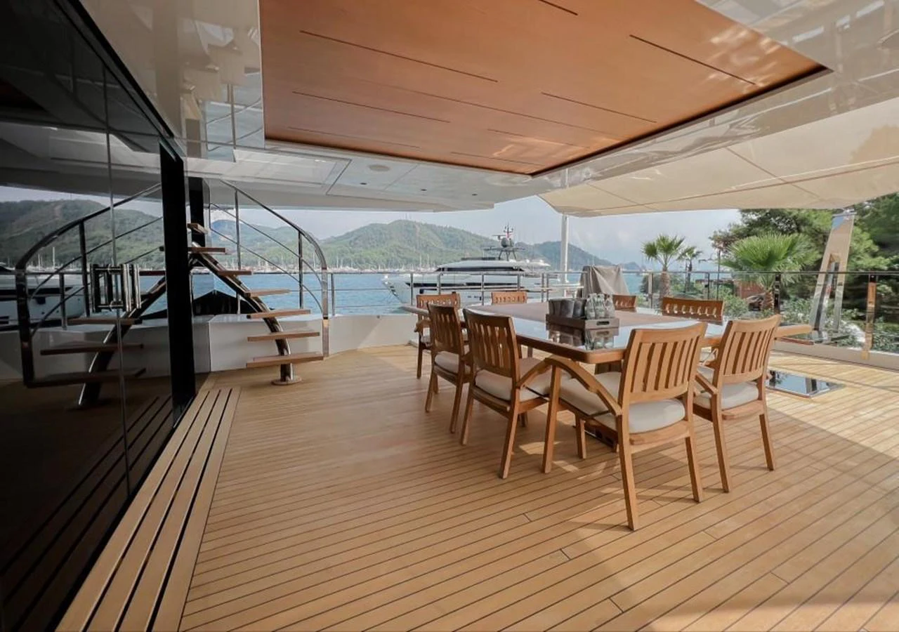 a wood table and chairs on a deck with a view of the water aboard UNASOLA Yacht for Sale