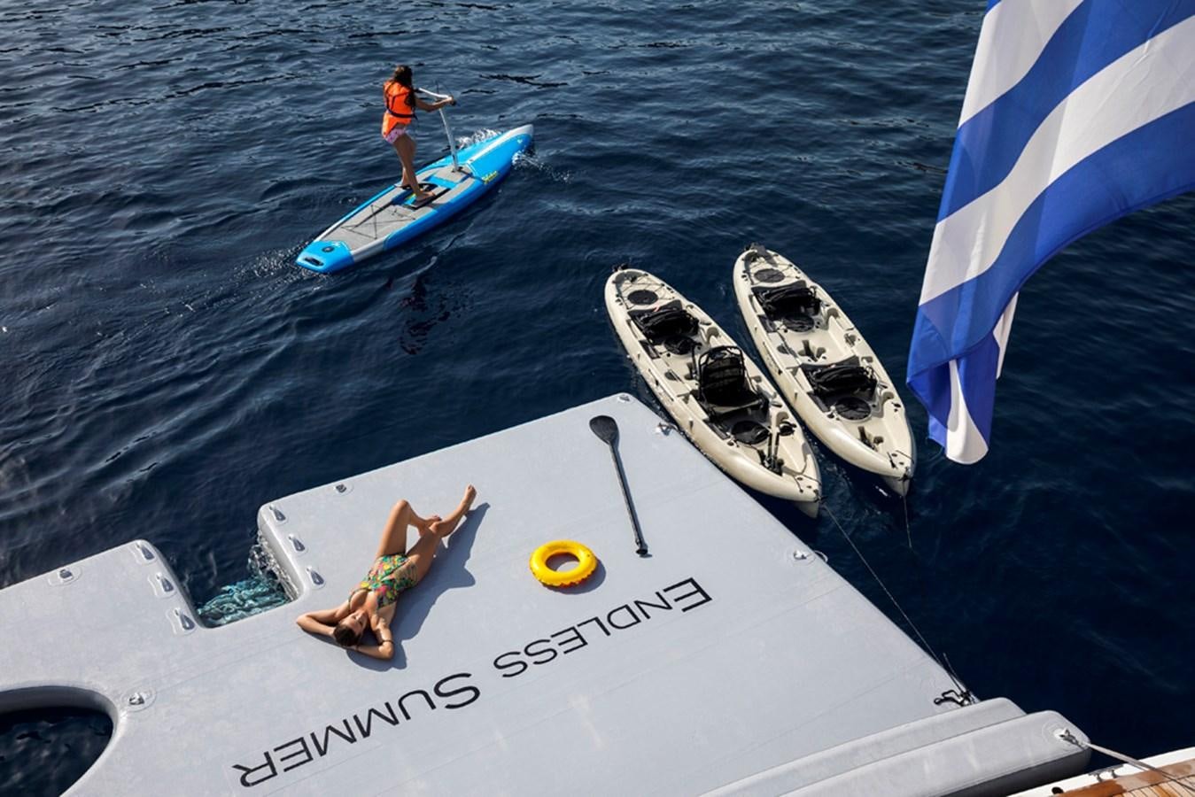 a person on a boat with a sail and a person on a surfboard aboard ENDLESS SUMMER Yacht for Sale