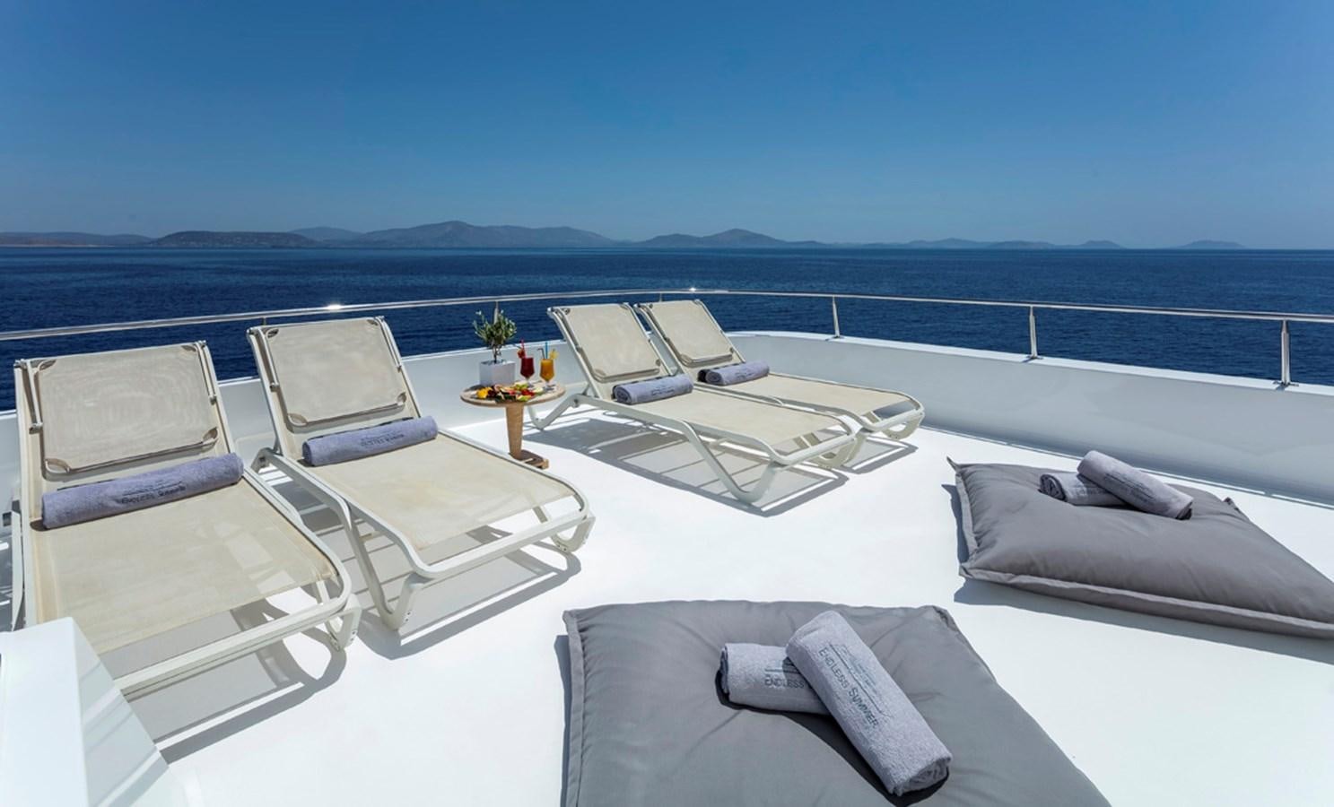 a white lounge chair on a white lounge chair on a beach with blue water and a blue sky aboard ENDLESS SUMMER Yacht for Sale
