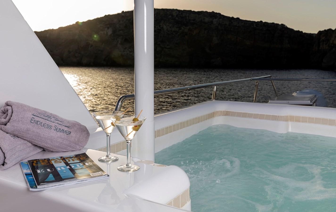 a book and glasses on a table by a pool aboard ENDLESS SUMMER Yacht for Sale
