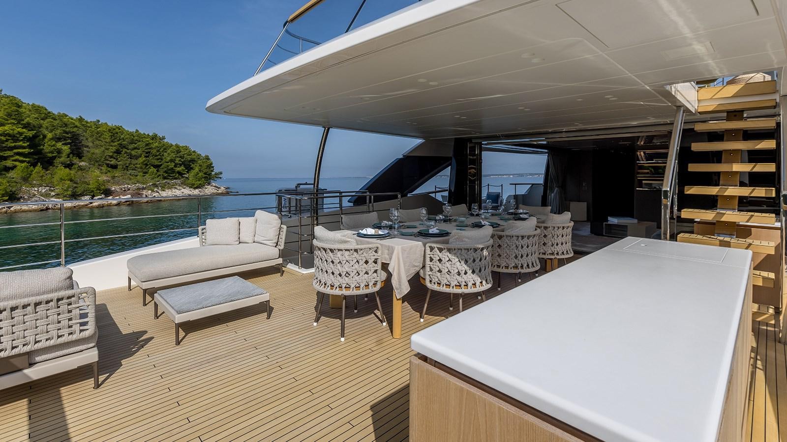 a lounge area with a table and chairs on a deck with a body of water and trees in aboard EROS Yacht for Sale