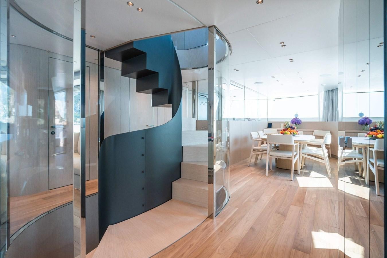 a room with a glass wall and a staircase with tables and chairs aboard AMI Yacht for Sale