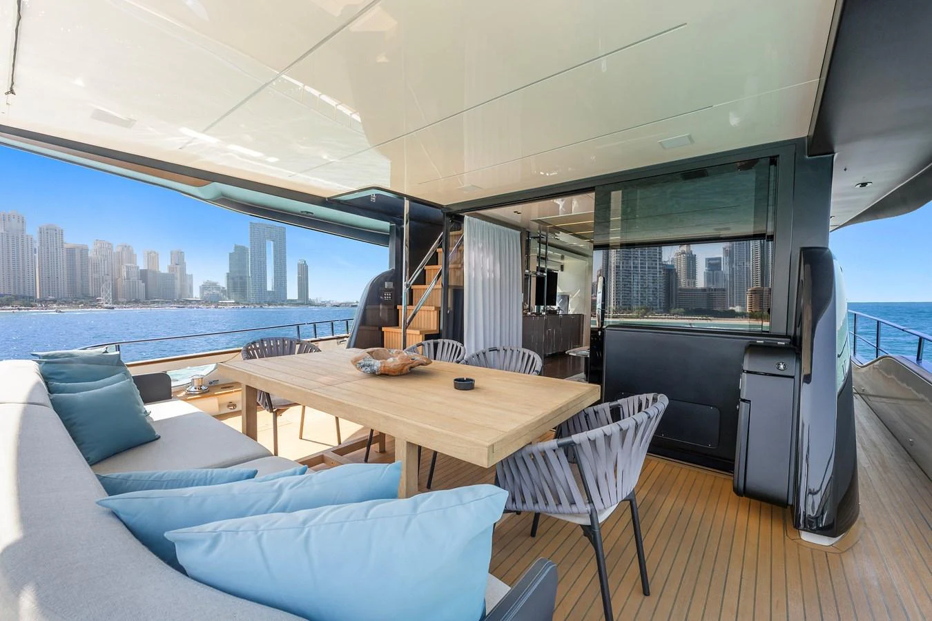 a room with a table and a couch and a large city in the background aboard MOSHE Yacht for Sale