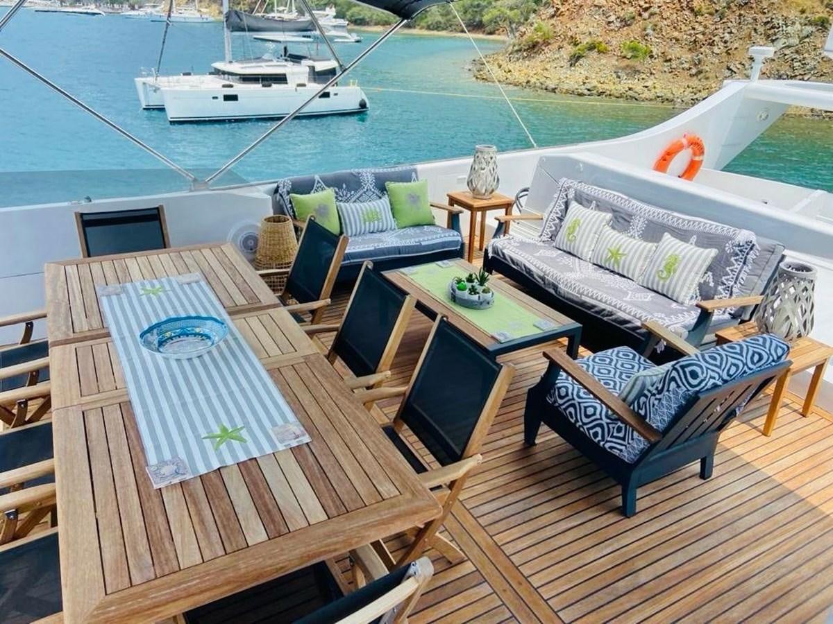 a deck with a table chairs and a boat in the background aboard THIRTY LOVE Yacht for Sale