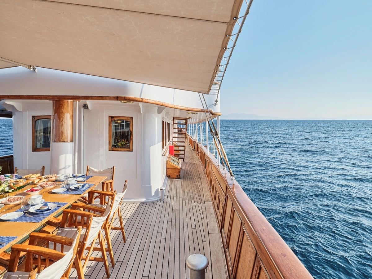 a deck with tables and chairs on it next to a body of water aboard MADIZ Yacht for Sale