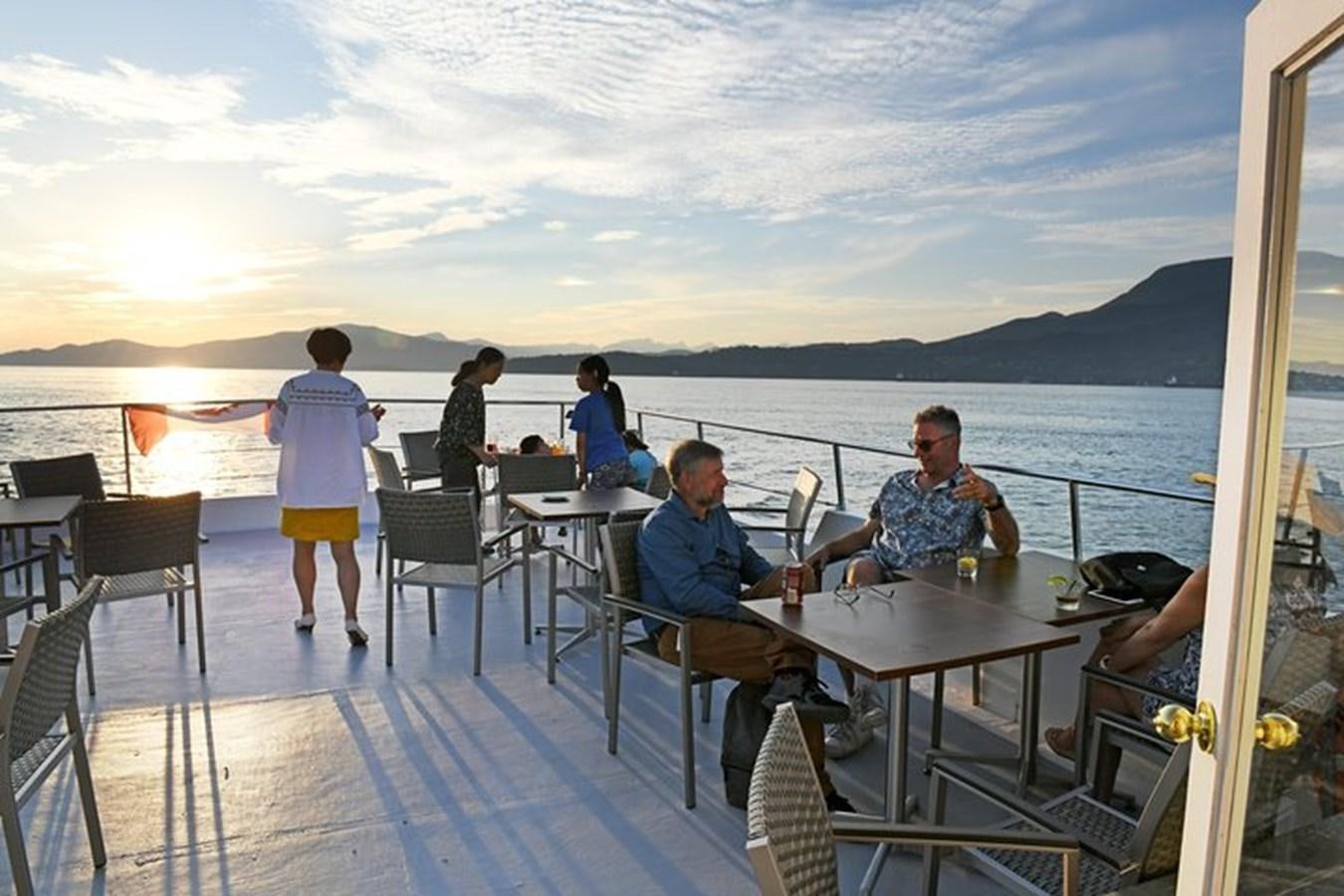 a group of people sitting at a table on a deck overlooking the ocean aboard 1990 PALMER MARINE 68 Yacht for Sale