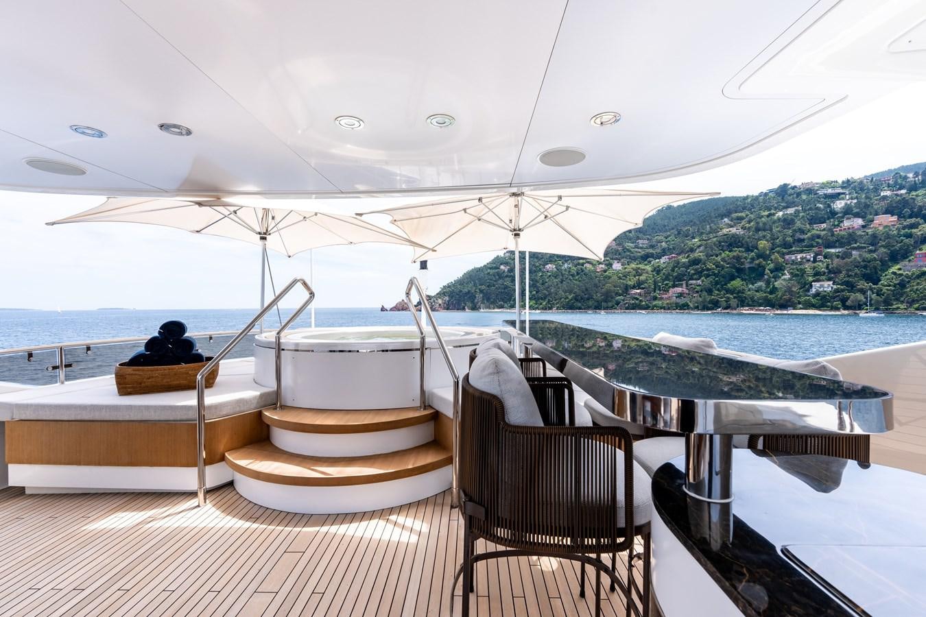 a deck with a chair and a table and a view of a body of water and mountains in aboard ANYA Yacht for Sale