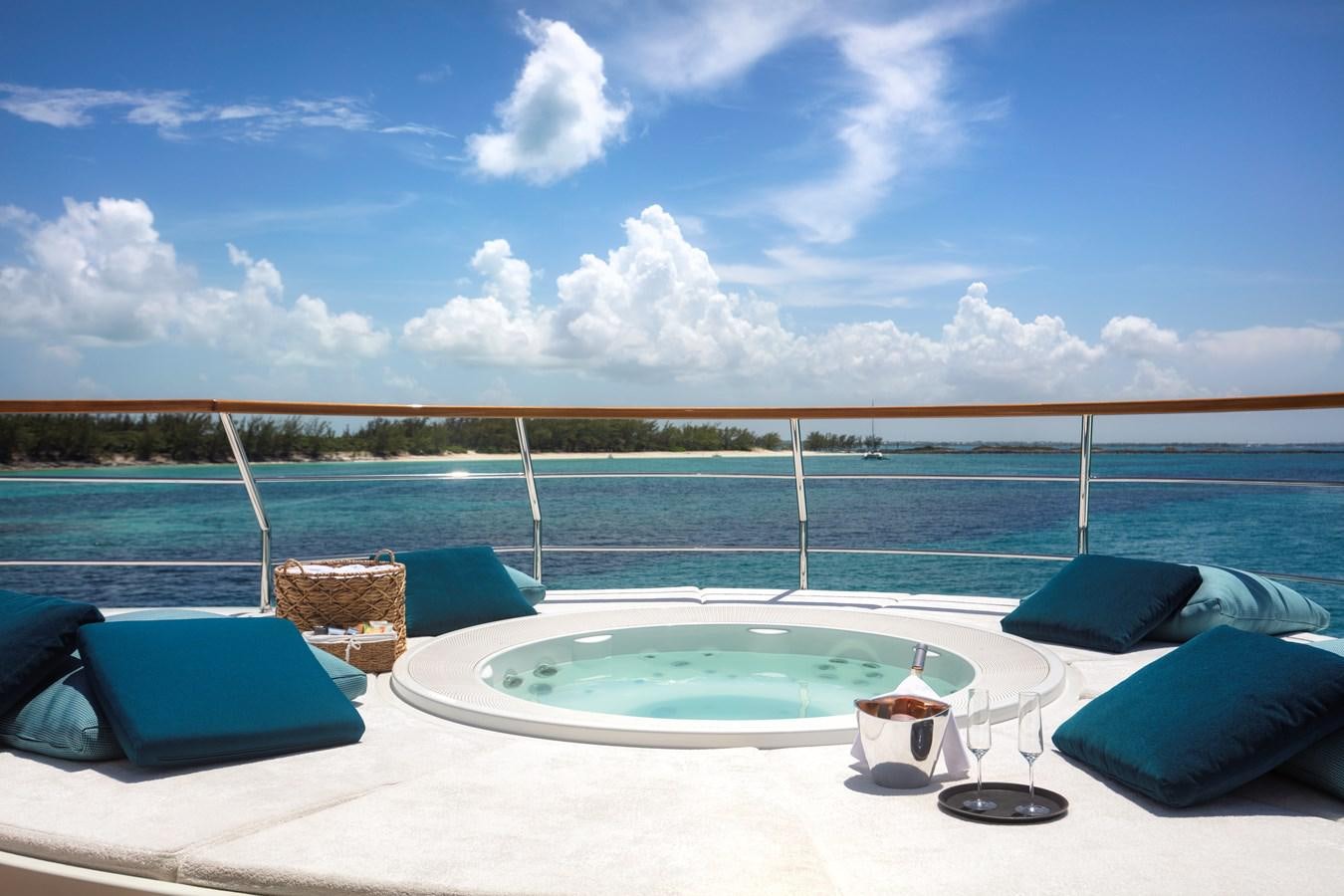 a pool with pillows and a table on a deck with a view of the water and blue sky aboard MYSTIC Yacht for Sale