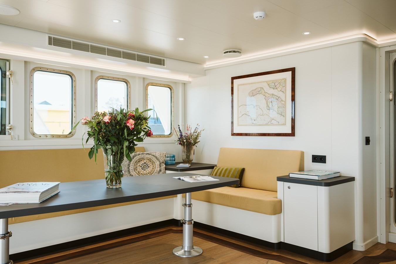 a living room with a yellow couch and a table with flowers aboard SCINTILLA MARIS Yacht for Sale