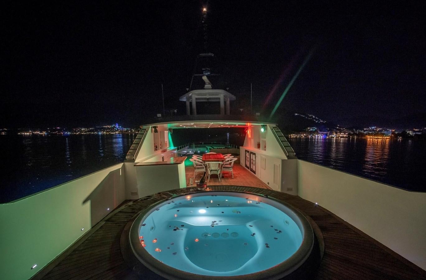 a pool with a table and chairs on a deck with a view of the water at night aboard ALKONOST Yacht for Sale