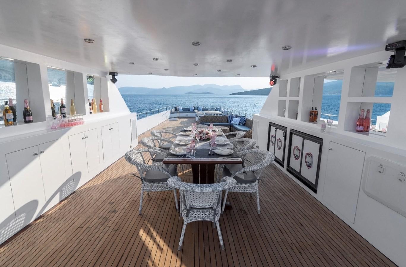 a dining table and chairs on a balcony overlooking a beach aboard ALKONOST Yacht for Sale