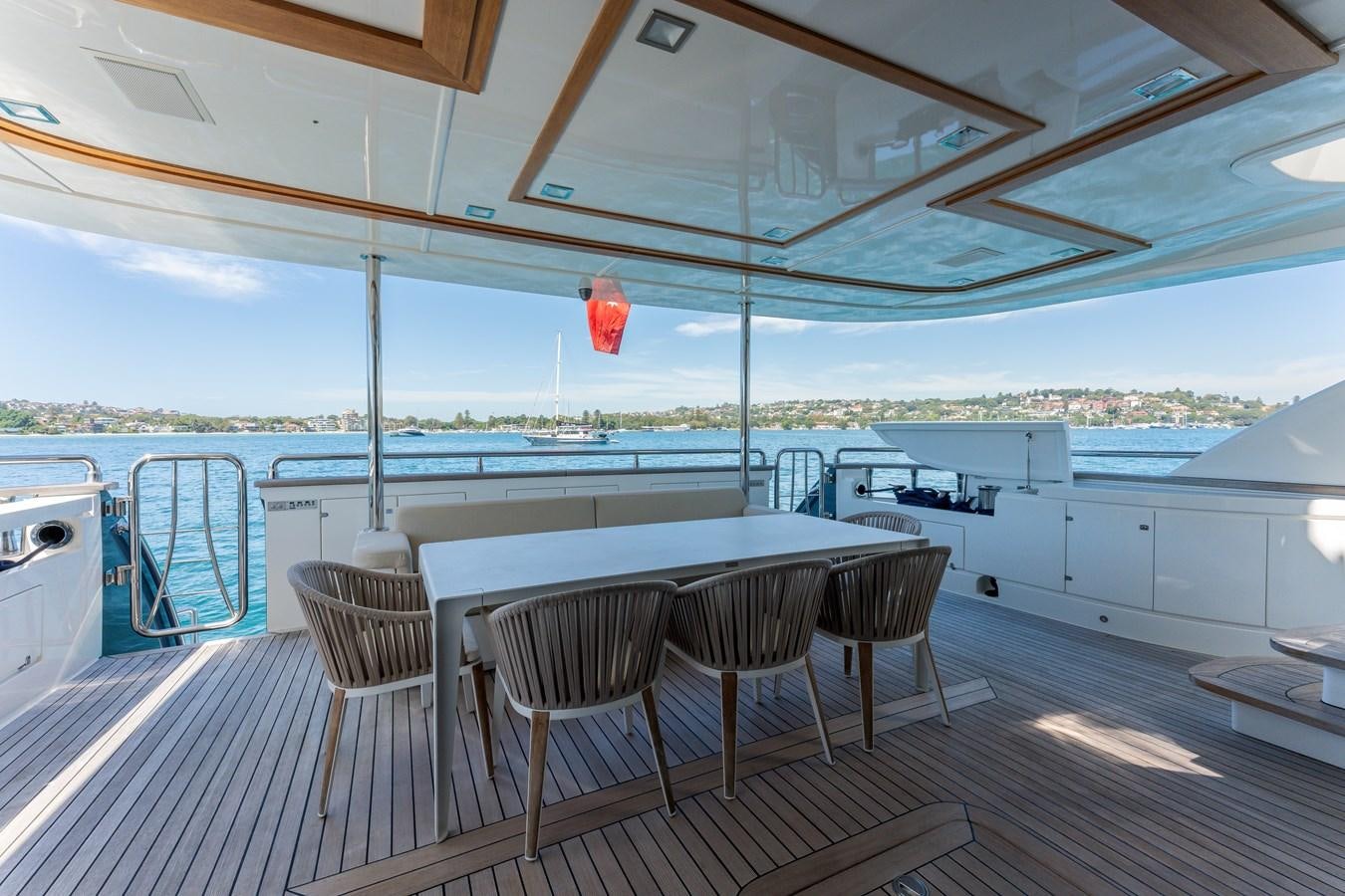 a large white table and chairs on a deck with a view of the water and a city in aboard DOMUS Yacht for Sale