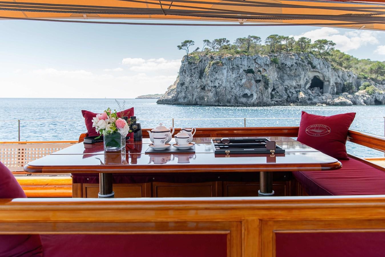 a table with chairs and a large rock in the background aboard MARIETTE OF 1915 Yacht for Sale