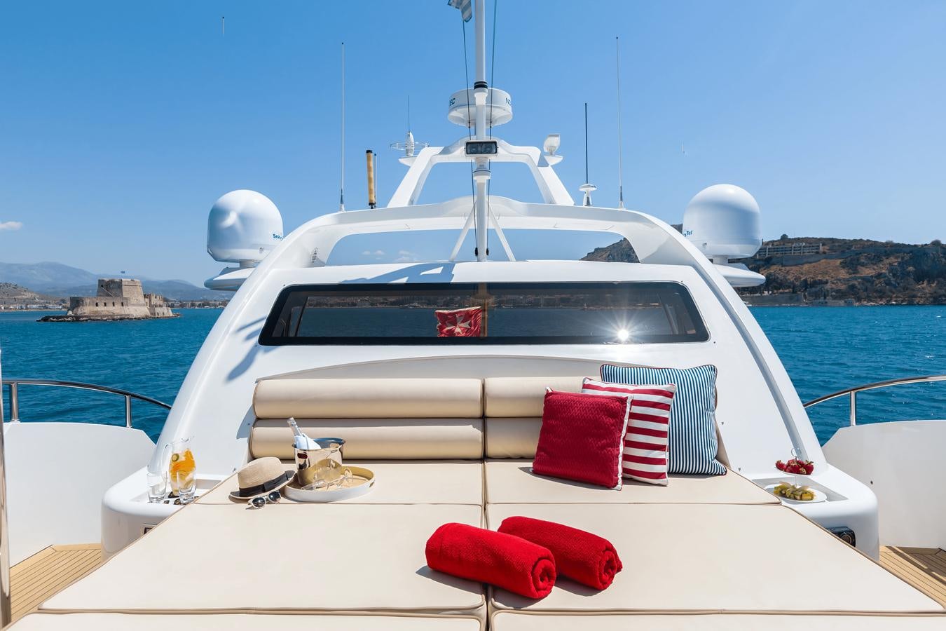 a white boat with red pillows on a white surface on a sunny day aboard REBECCA V Yacht for Sale