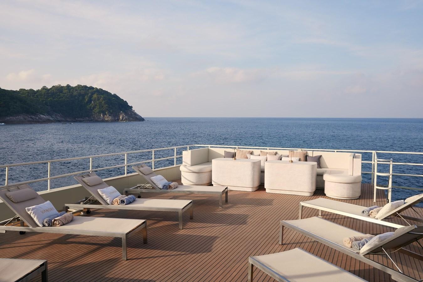 a boat dock with lounge chairs and a body of water in the background aboard VANORA Yacht for Sale