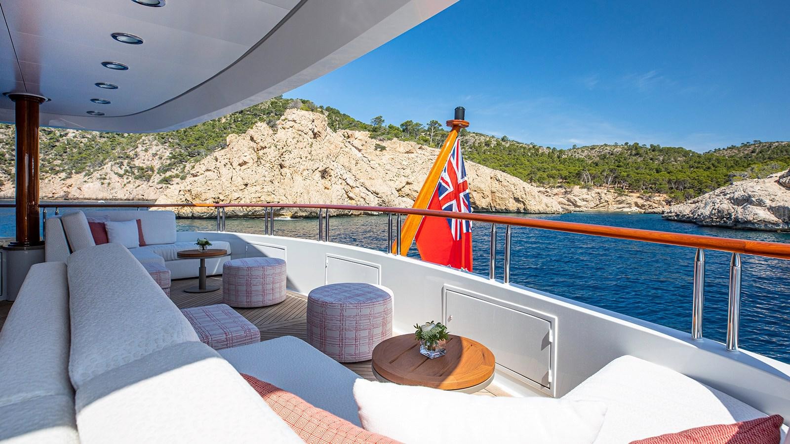 a deck with a large pool and a beach and mountains in the background aboard LA DEA II Yacht for Sale