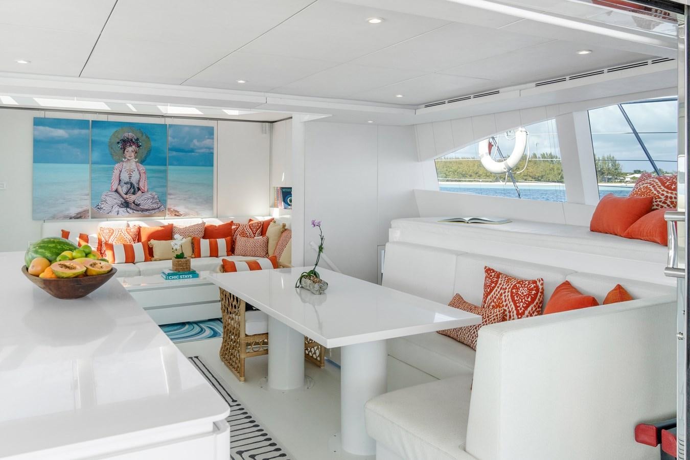 a white living room with a white table and orange pillows aboard ROYAL RITA Yacht for Sale