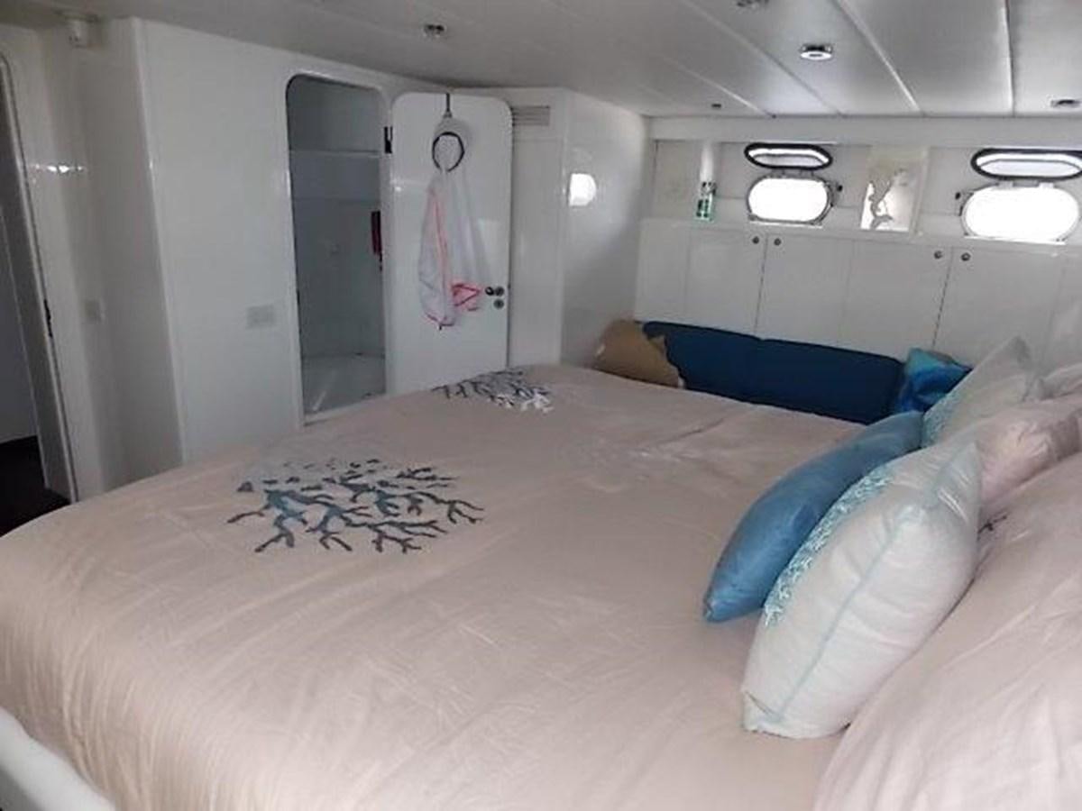 a bed with a white sheet and a blue pillow on it aboard PACIFIC PEARL Yacht for Sale