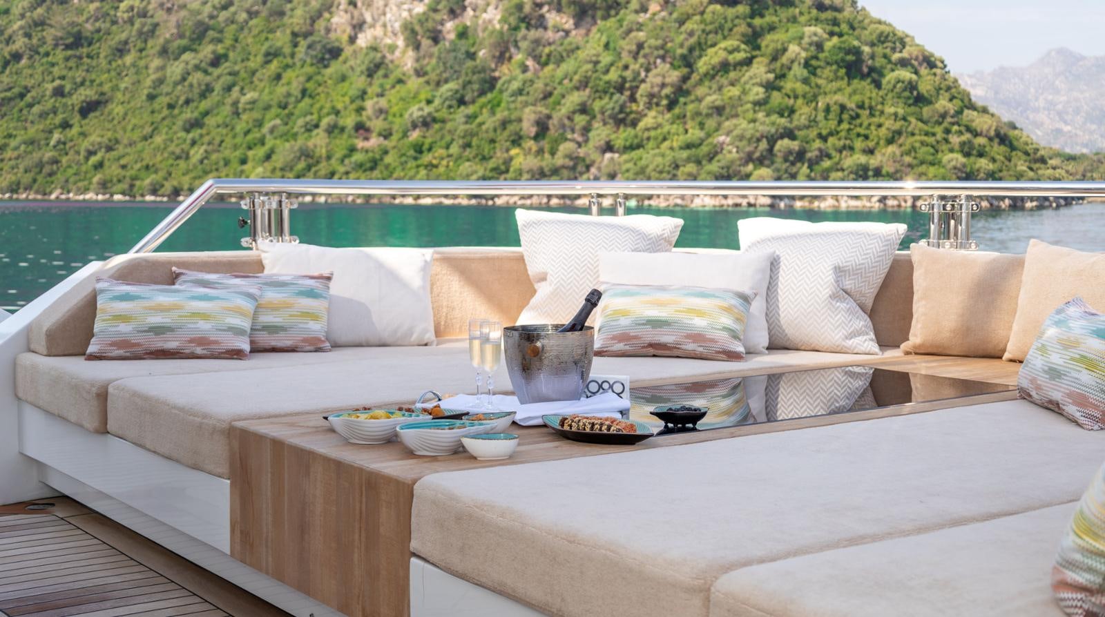 a white couch with a table and a white coffee table with a view of mountains and trees in aboard M 47 Yacht for Sale